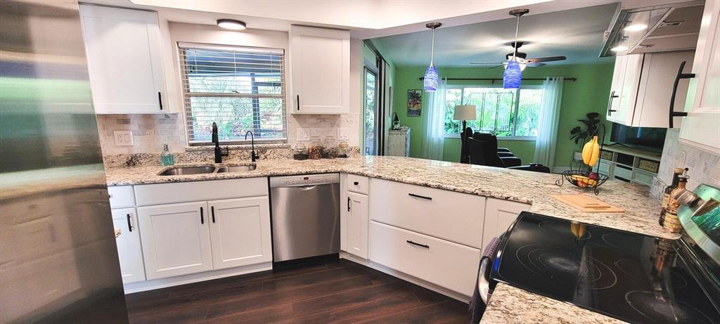 A kitchen features white cabinets, granite countertops, stainless steel appliances, and dark wood flooring — 755 KENT ROAD, VENICE, FL