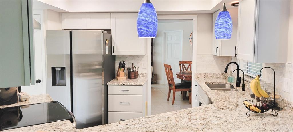 A kitchen features white cabinets, granite countertops, stainless steel appliances, and two blue pendant lights — 755 KENT ROAD, VENICE, FL