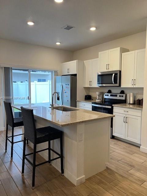 A kitchen features white cabinets, a granite-topped island with two barstools, and wood-look flooring — HOMESTEAD, FL