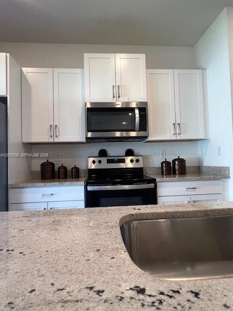 A kitchen features white cabinets, stainless steel appliances, and light-colored granite countertops — HOMESTEAD, FL