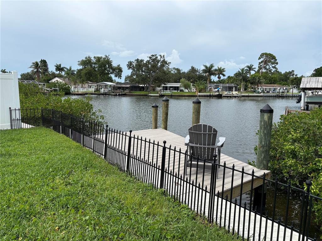 A wooden dock with a chair sits on a canal behind a black metal fence — 4820 VENETIAN BOULEVARD NE, ST PETERSBURG, FL