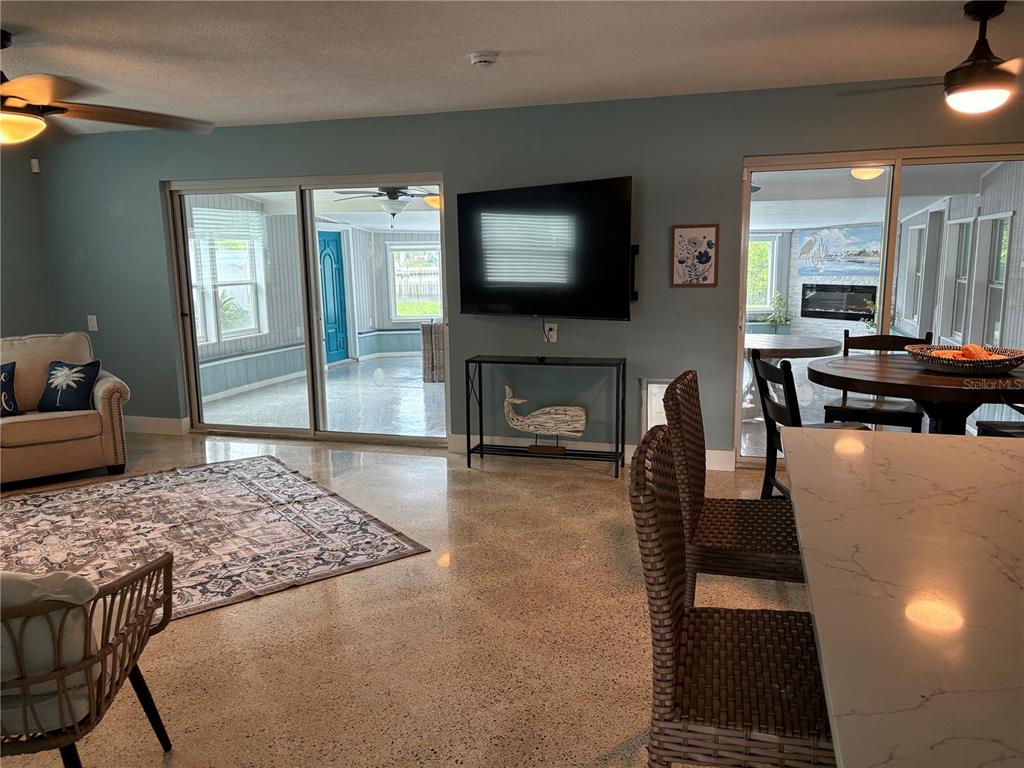 A living room with polished concrete floors, a wall-mounted television, and sliding glass doors — 4820 VENETIAN BOULEVARD NE, ST PETERSBURG, FL