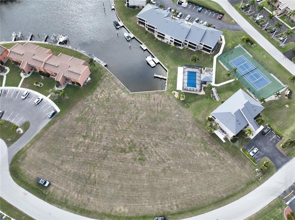 An aerial view shows a vacant lot situated between a canal, parking areas, and buildings — 1341 ROCK DOVE COURT, PUNTA GORDA, FL