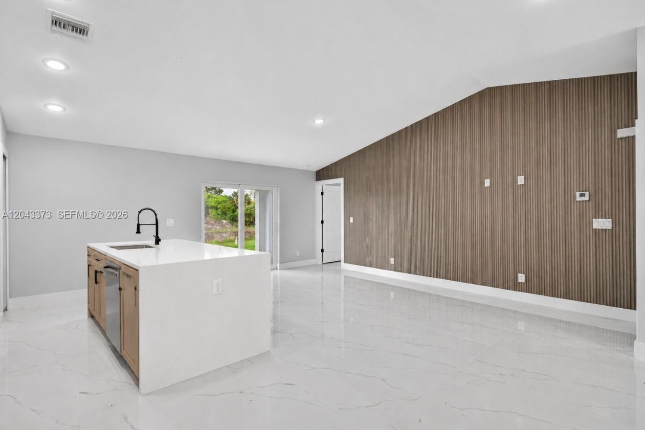 A kitchen island with a white countertop sits in a room with wood-slatted accent walls — 1871 Tobin st, Lehigh Acres FL 33972, LEHIGH ACRES, FL