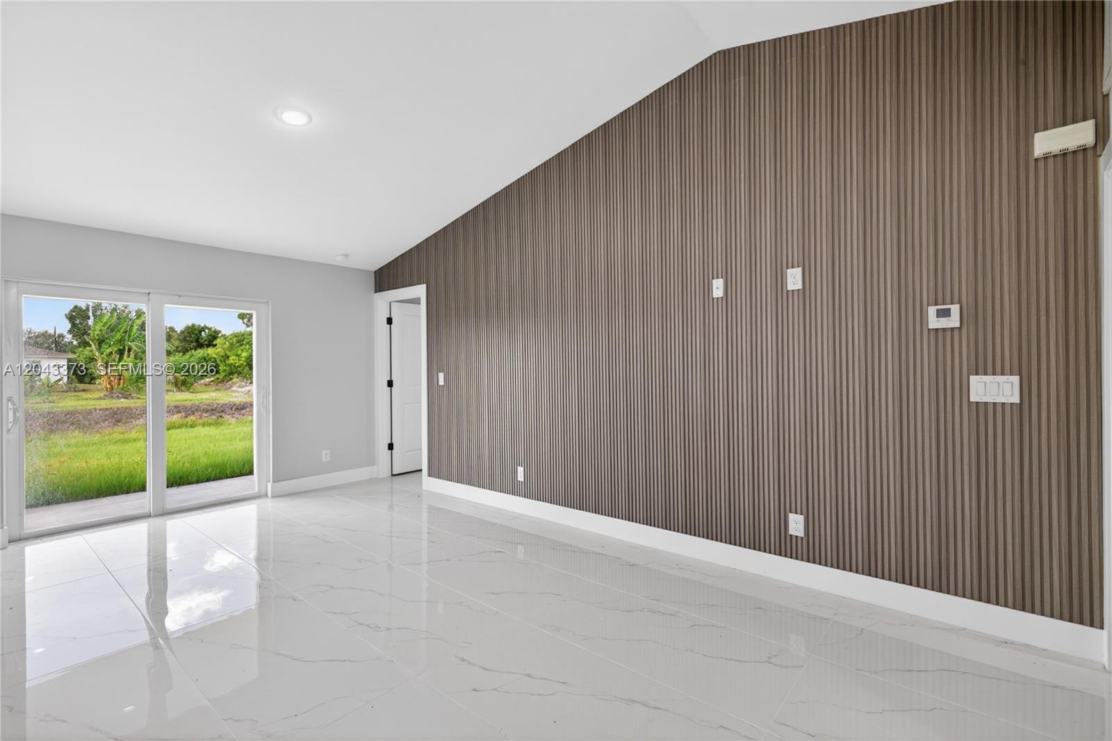 A room with white marble floors, a slatted wood accent wall, and sliding glass doors — 1871 Tobin st, Lehigh Acres FL 33972, LEHIGH ACRES, FL