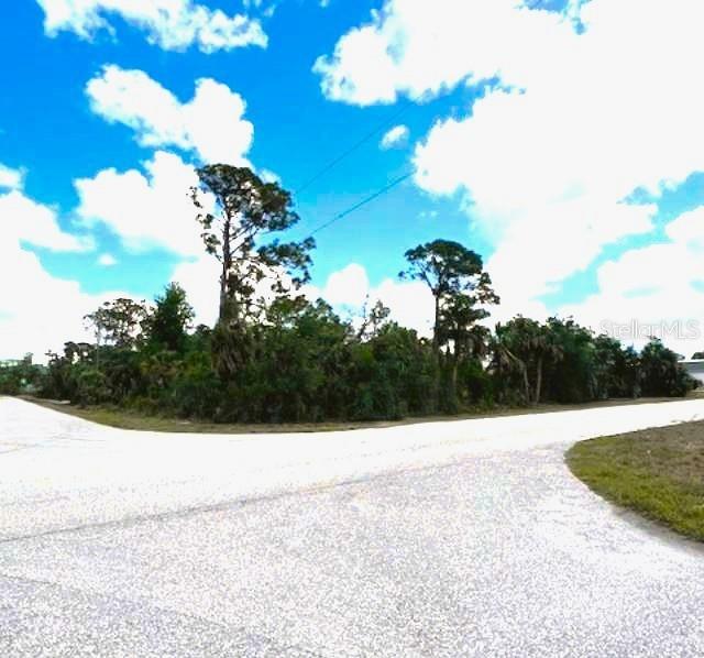 A paved road intersection sits in front of a wooded lot with tall pine trees — 17128 WINTERGARDEN AVENUE, PORT CHARLOTTE, FL