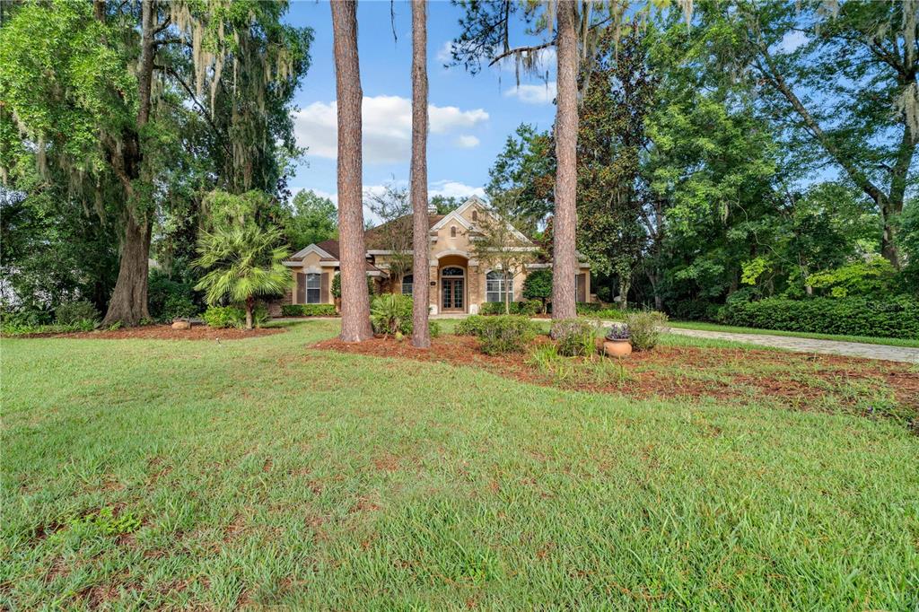 A single-story house with a beige facade sits behind tall pine trees and green lawn — 5038 SE 6TH AVENUE, OCALA, FL