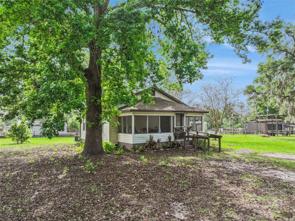 A small, light-colored house with a screened-in porch sits under a large oak tree — 4125 LAVON REYNOLDS LANE, LAKELAND, FL
