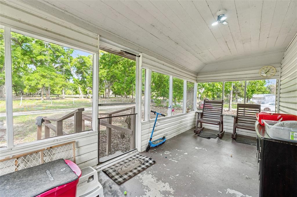 A screened-in porch features white walls, a concrete floor, two rocking chairs, and outdoor views — 4125 LAVON REYNOLDS LANE, LAKELAND, FL
