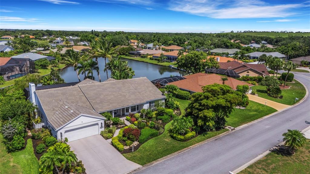 An aerial view of a suburban house with a tile roof, driveway, and backyard pond — 5679 COUNTRY LAKES DRIVE UNIT 7, SARASOTA, FL