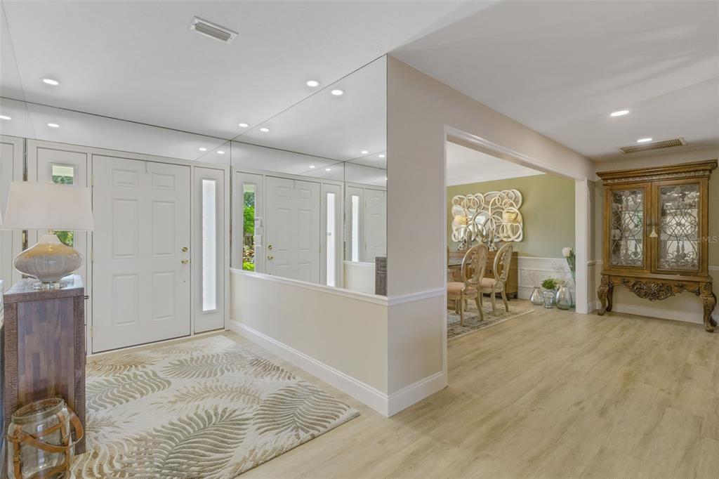 An entryway with a mirrored wall, light wood flooring, and a view into the dining room — 5679 COUNTRY LAKES DRIVE UNIT 7, SARASOTA, FL