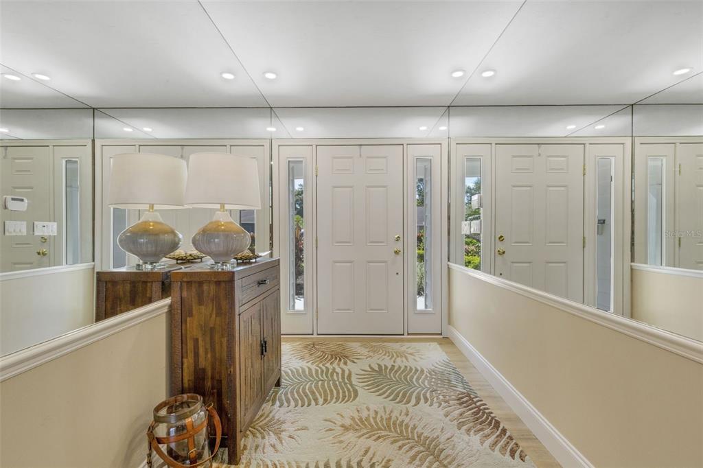 An entryway features a wooden cabinet, two lamps, a patterned rug, and mirrored walls — 5679 COUNTRY LAKES DRIVE UNIT 7, SARASOTA, FL