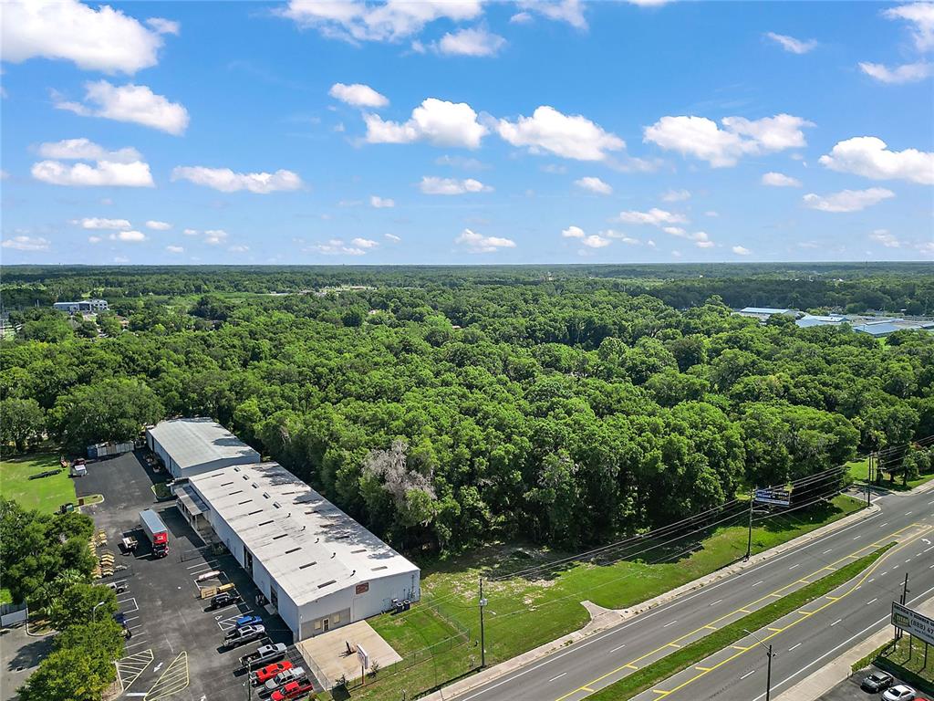 An aerial view shows a commercial warehouse building next to a road and dense trees — 2105 NW 10TH (US HWY 27) STREET, OCALA, FL