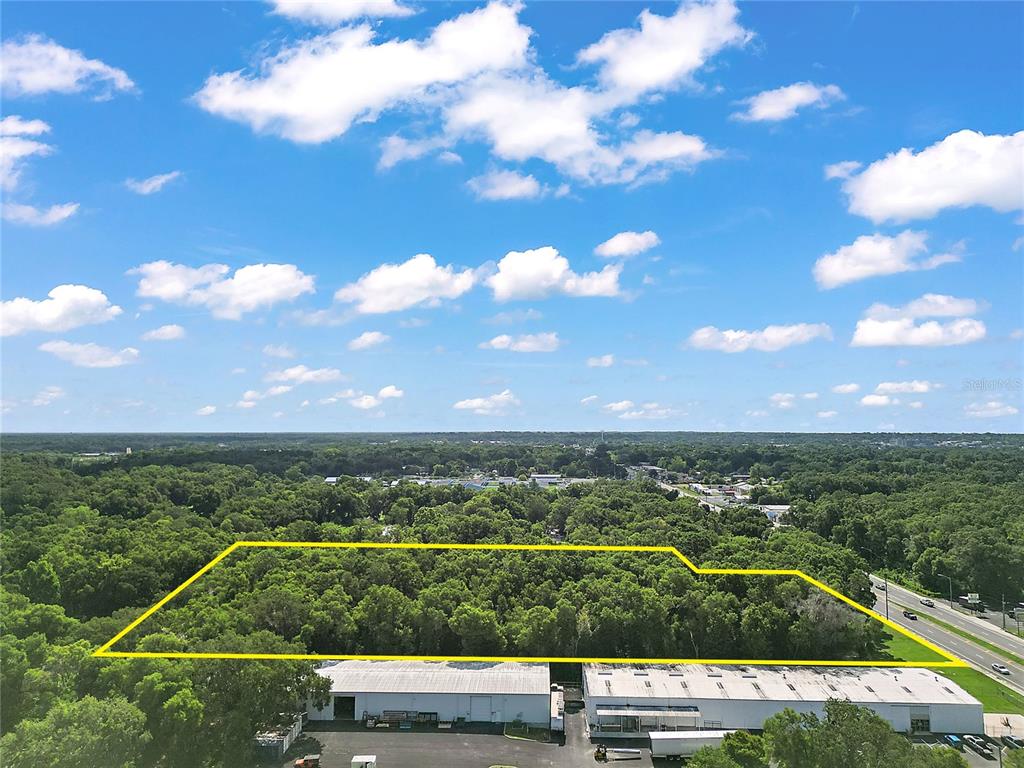 An aerial view shows a wooded lot outlined in yellow adjacent to a commercial building — 2105 NW 10TH (US HWY 27) STREET, OCALA, FL