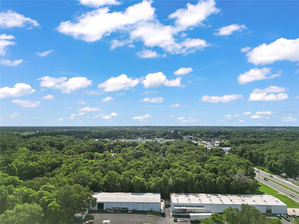 An aerial view shows two industrial warehouse buildings surrounded by dense trees under a cloudy sky — 2105 NW 10TH (US HWY 27) STREET, OCALA, FL