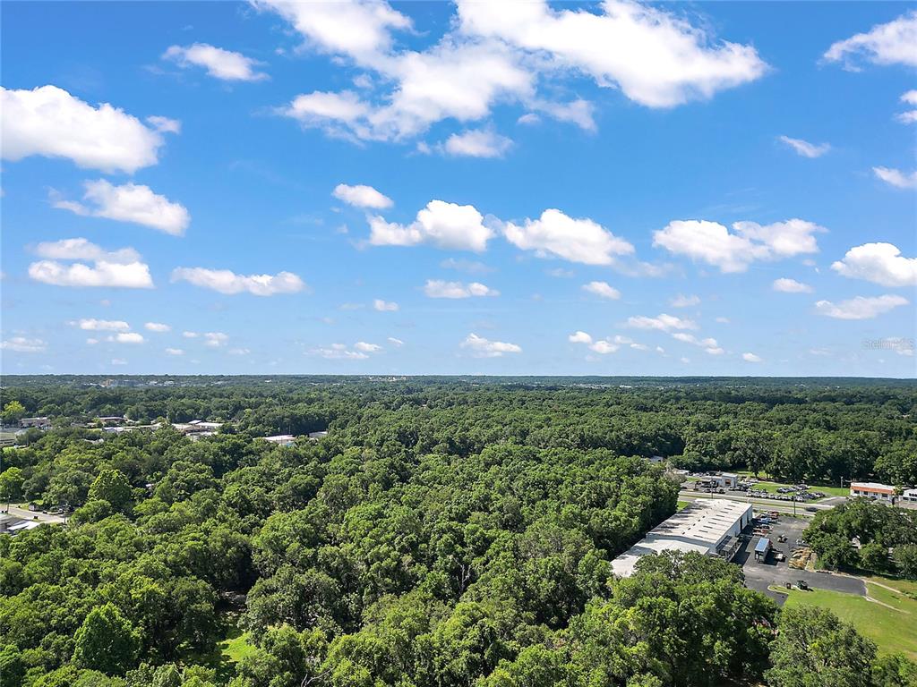 An aerial view shows a dense forest landscape under a bright blue sky with clouds — 2105 NW 10TH (US HWY 27) STREET, OCALA, FL
