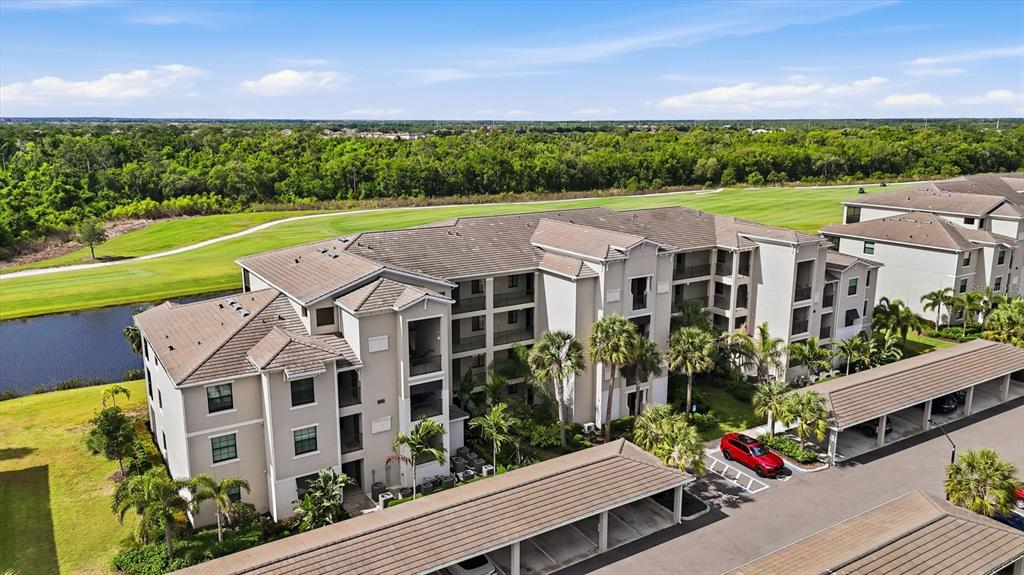 An aerial view shows a multi-story apartment building with a parking structure and golf course — 18008 GAWTHROP DRIVE UNIT 401, BRADENTON, FL