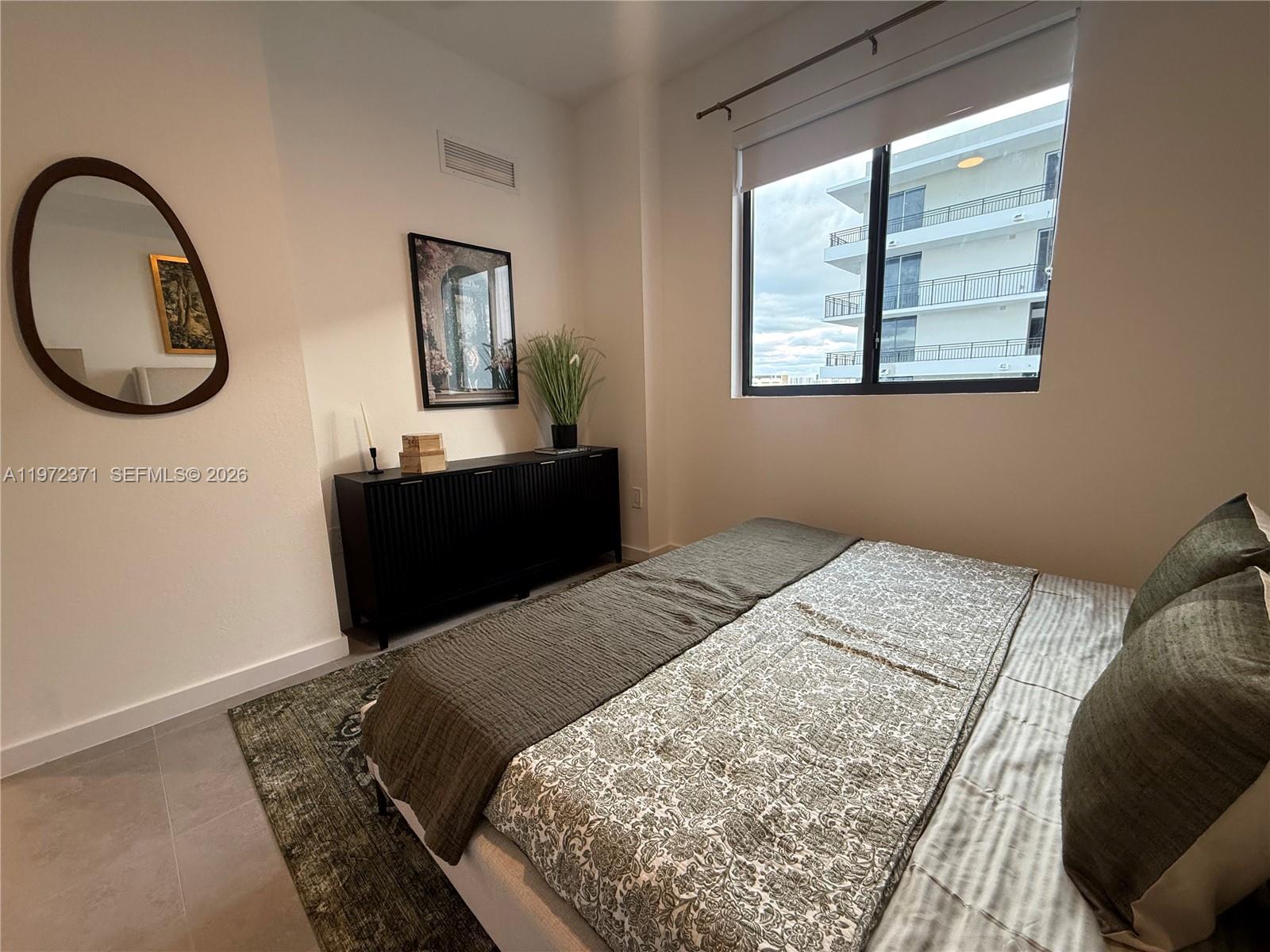 A bedroom features a bed, a black sideboard, a wall mirror, and a window view — 2001 Van Buren St # 545, Hollywood FL 33020, HOLLYWOOD, FL