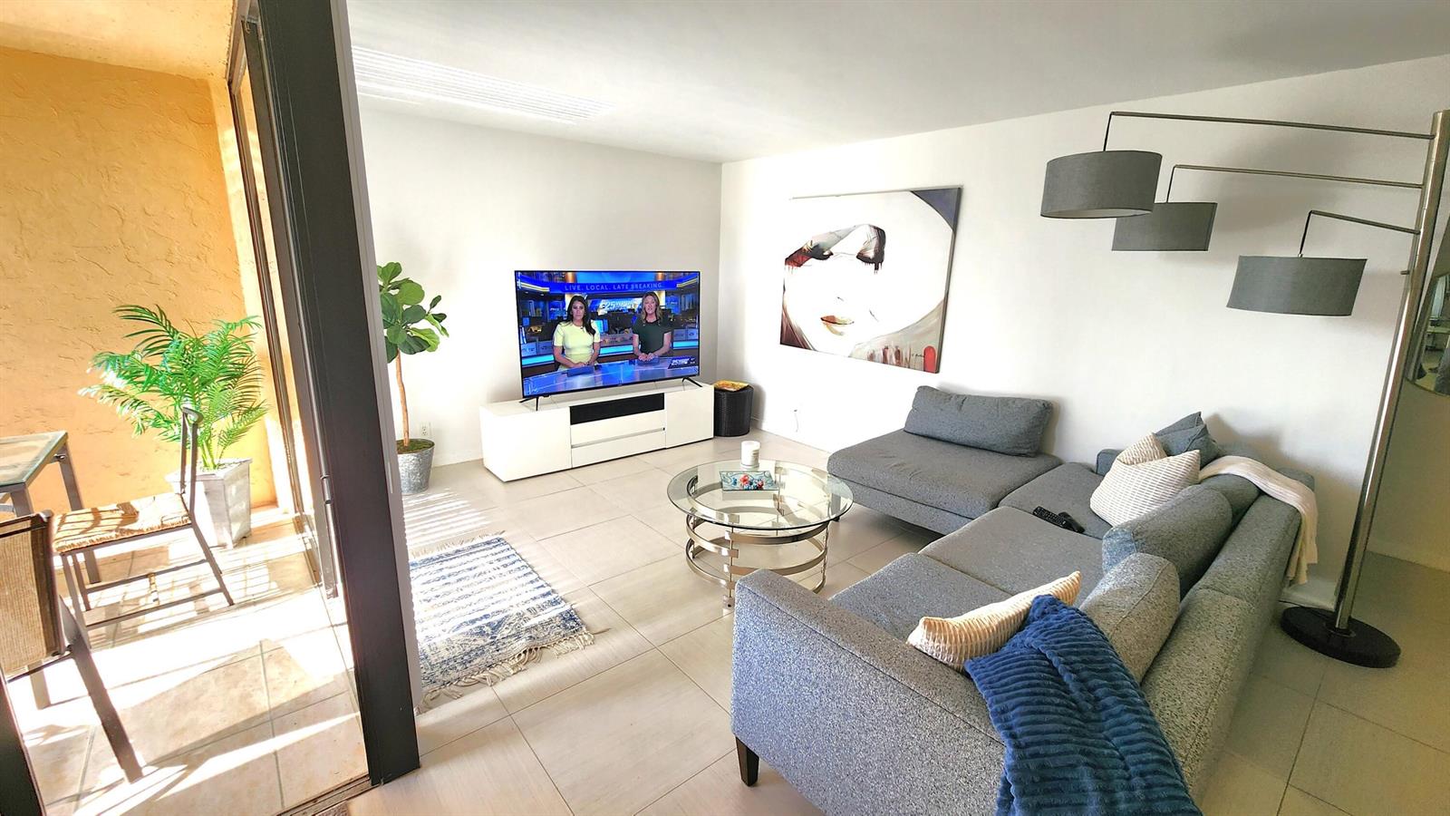 A living room features a gray sectional sofa, glass coffee table, television, and a balcony — 2255 Lindell Boulevard # 4303, Delray Beach FL 33444, DELRAY BEACH, FL