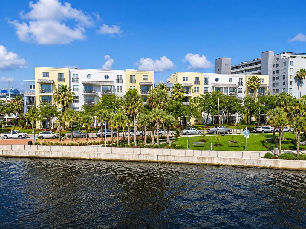 A multi-story apartment complex sits along a waterfront with palm trees and parked cars — 1501 DOYLE CARLTON DRIVE UNIT 411, TAMPA, FL