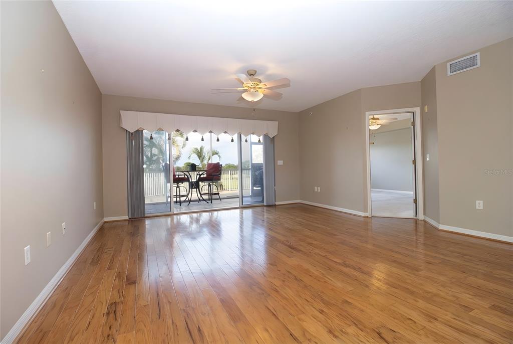 An empty living room features hardwood floors, a ceiling fan, and sliding glass doors to a balcony — 1200 COUNTRY CLUB DRIVE UNIT 1101, LARGO, FL