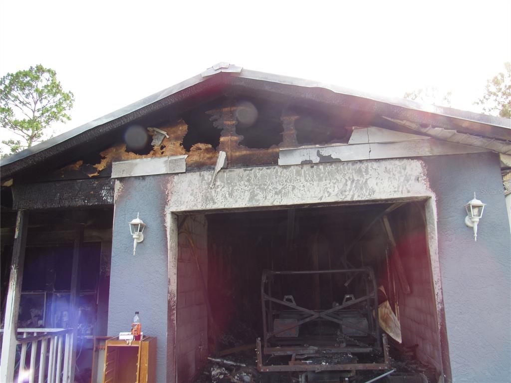 A fire-damaged garage exterior with charred roof framing and debris visible inside — 5620 SW 181ST COURT, DUNNELLON, FL