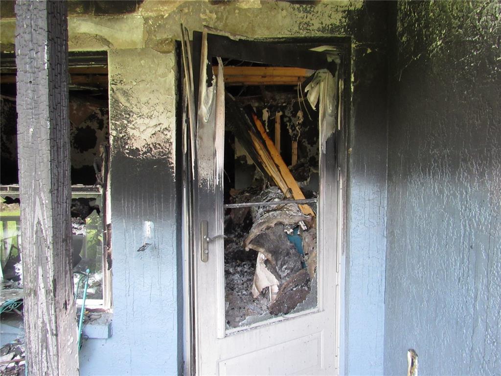 A severely fire-damaged exterior doorway and wall with charred wood and debris visible inside — 5620 SW 181ST COURT, DUNNELLON, FL