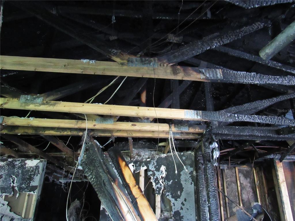 A view of a fire-damaged room interior showing charred wooden ceiling trusses and exposed wiring — 5620 SW 181ST COURT, DUNNELLON, FL