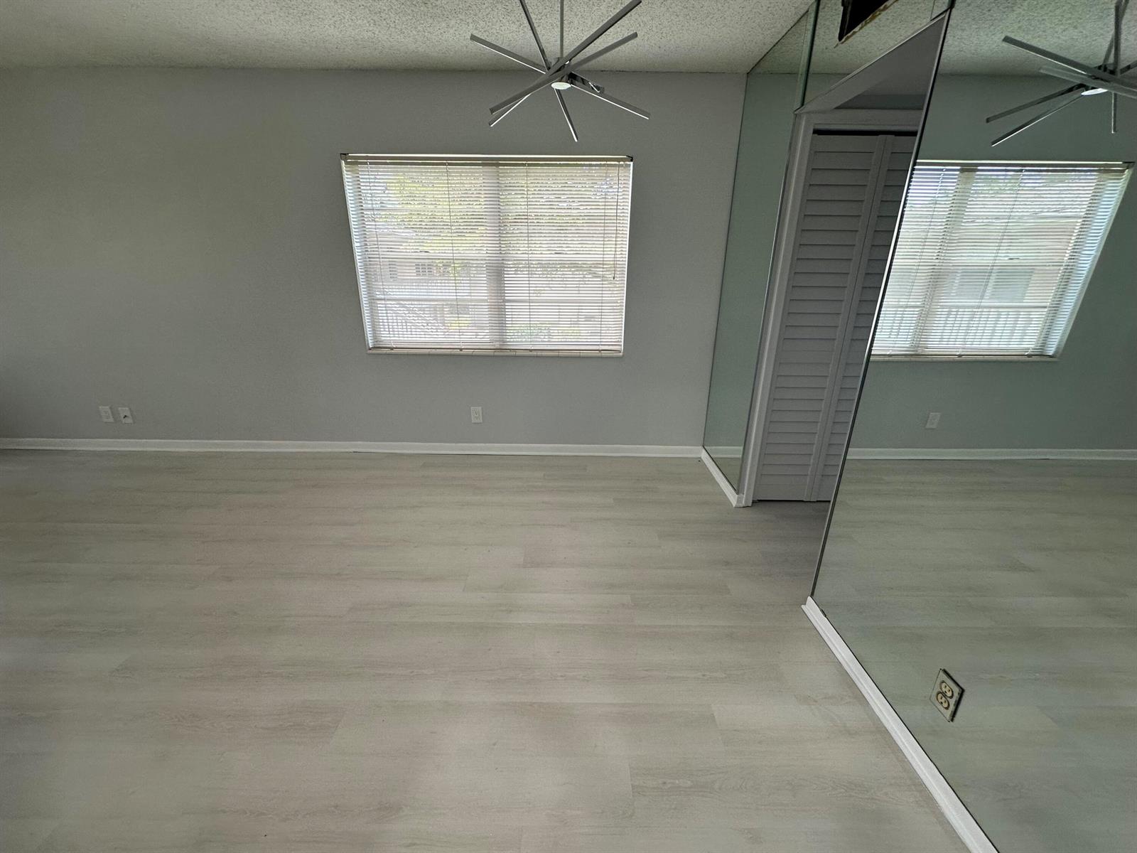 An empty room features light gray wood-look flooring, a window with blinds, and mirrored walls — 21 Salisbury A, West Palm Beach FL 33417, WEST PALM BEACH, FL