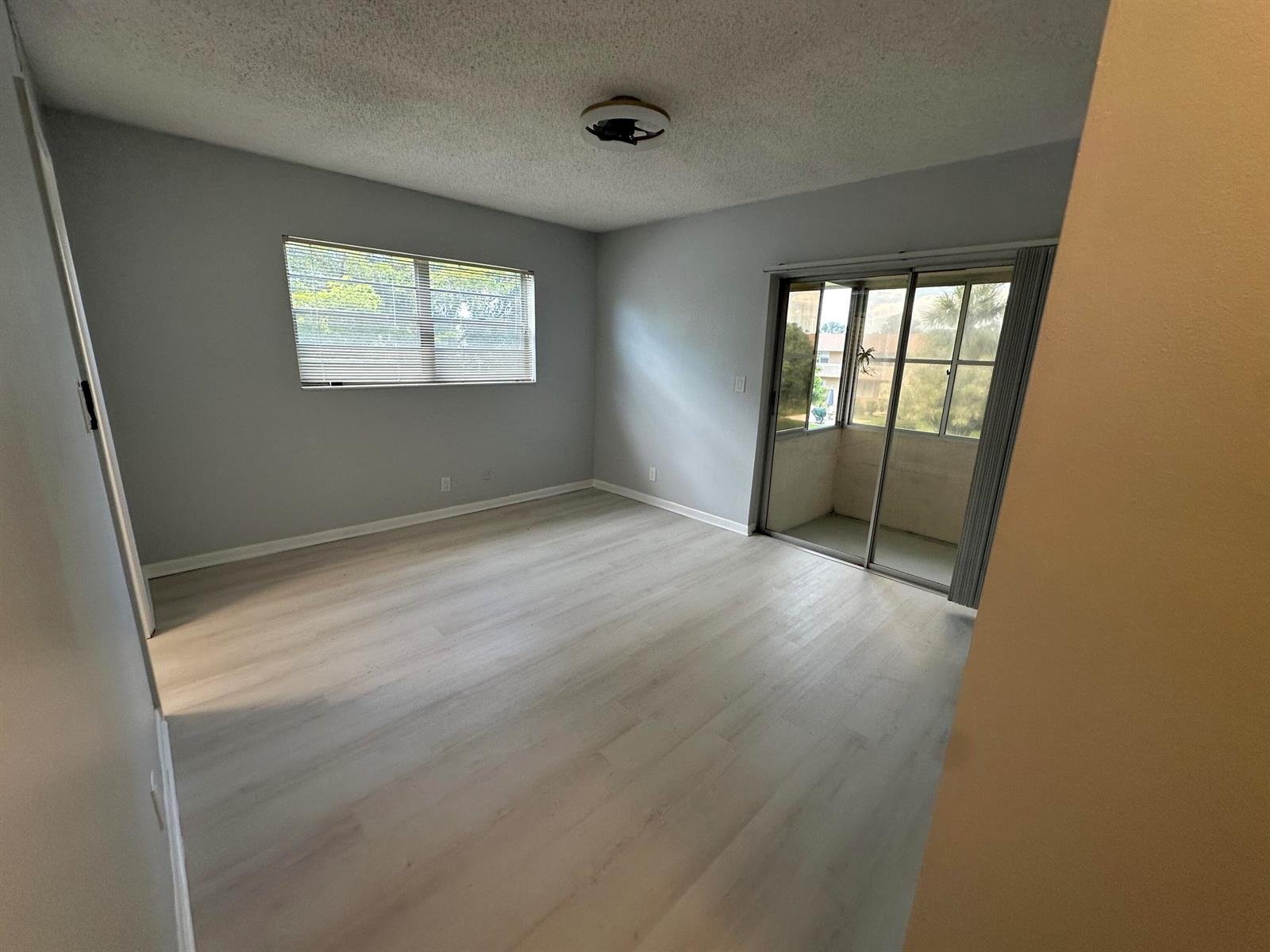 An empty room features light gray walls, wood-look flooring, a window, and a sliding glass door — 21 Salisbury A, West Palm Beach FL 33417, WEST PALM BEACH, FL