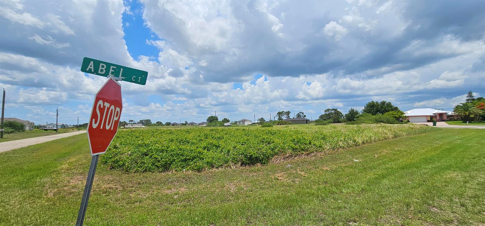 A stop sign and street sign for Abel Ct stand before a vacant, grassy lot — 9008 Abel Court, FL 33935, FL