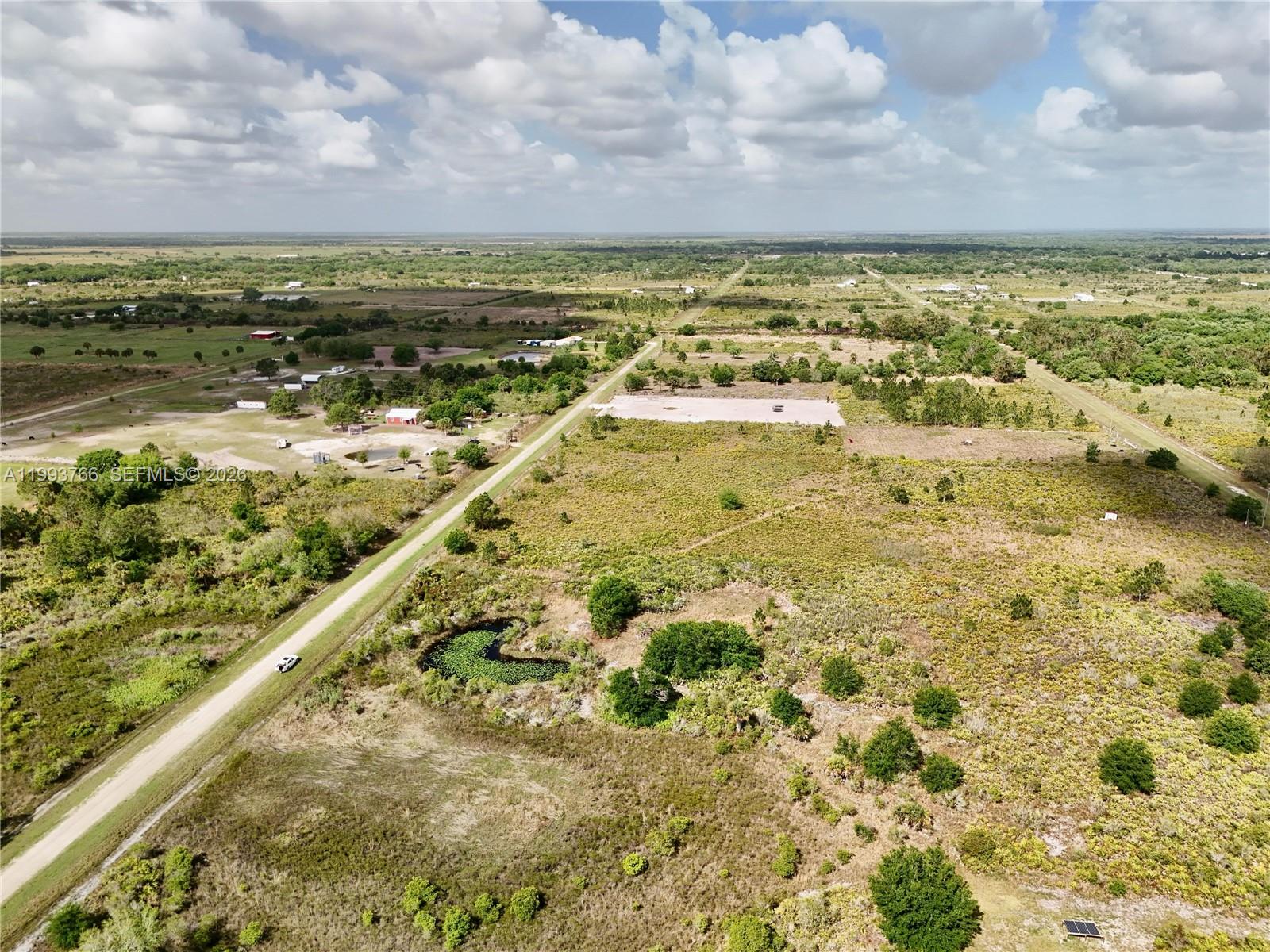 An aerial view shows a rural landscape with a dirt road, vegetation, and a pond — 17923 NW 250TH, Okeechobee FL 34972, OKEECHOBEE, FL