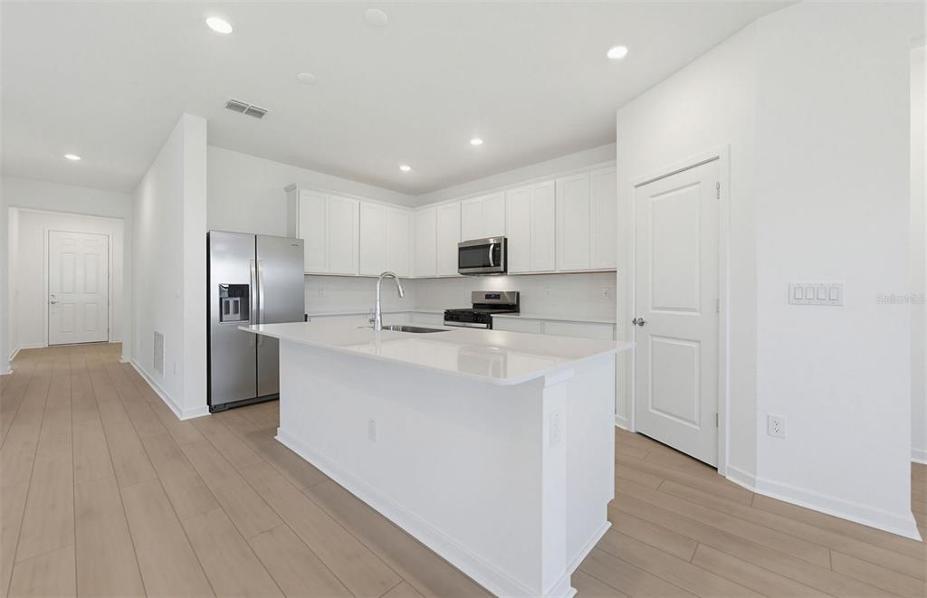 A modern kitchen features white cabinets, stainless steel appliances, a center island, and light flooring — 33383 HERDS HALLOW WAY, WESLEY CHAPEL, FL