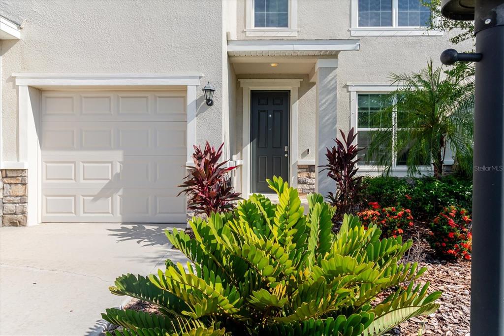 A beige two-story house exterior features a single-car garage, a dark front door, and landscaping — 16725 BARNWOOD PLACE, BRADENTON, FL