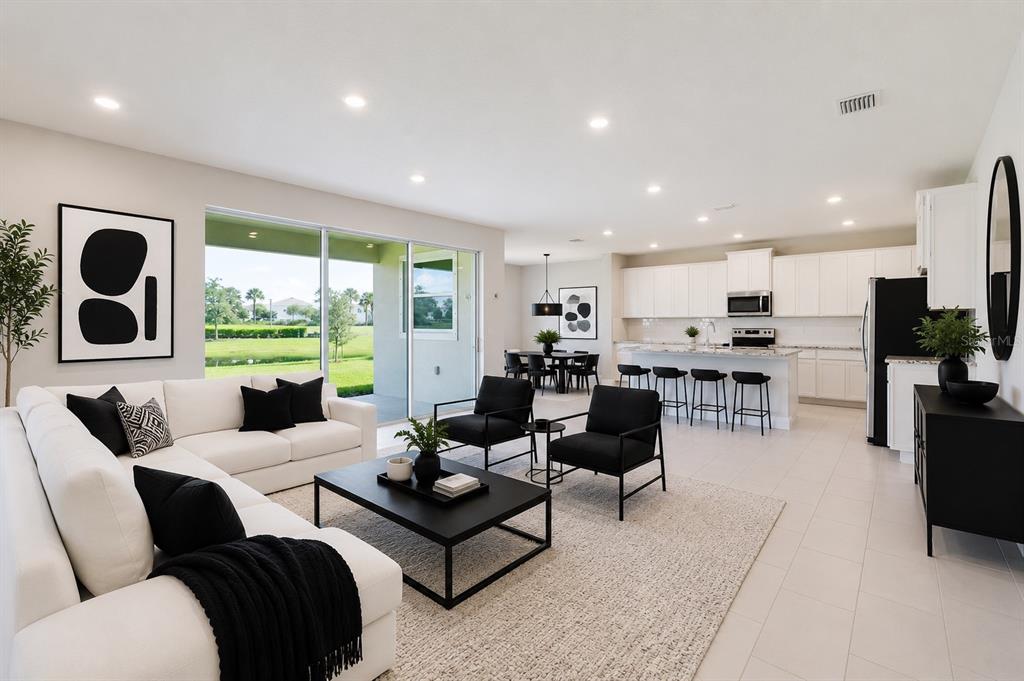 An open-concept living room and kitchen feature white cabinetry, black accents, and large sliding doors — 16725 BARNWOOD PLACE, BRADENTON, FL