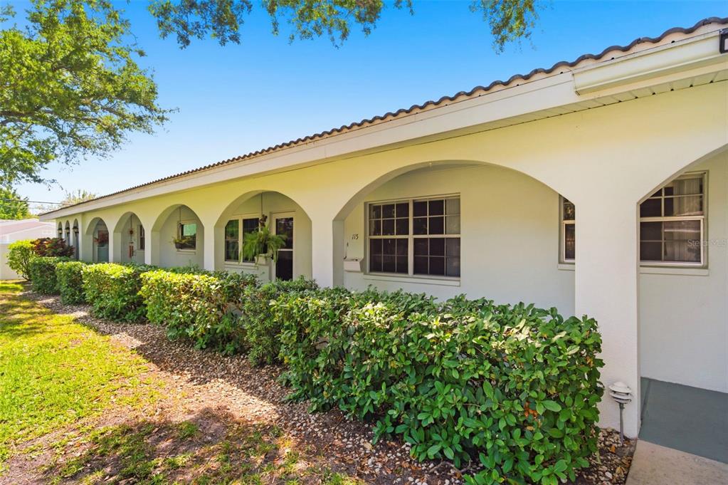 A white exterior wall features a covered walkway with arched openings and a manicured hedge — 11200 102ND AVENUE UNIT 115, SEMINOLE, FL