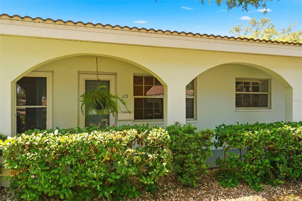 A white house exterior features a covered entryway with arched openings and a front door — 11200 102ND AVENUE UNIT 115, SEMINOLE, FL
