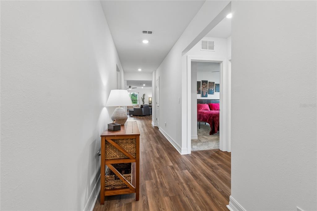A hallway with wood-look flooring leads to a living area, with a bedroom visible nearby — 3883 CAPRI COAST DRIVE, PLANT CITY, FL