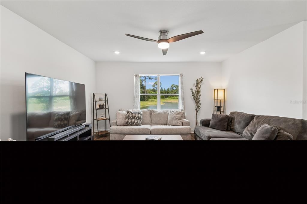 A living room features a ceiling fan, a large television, and a window overlooking water — 3883 CAPRI COAST DRIVE, PLANT CITY, FL