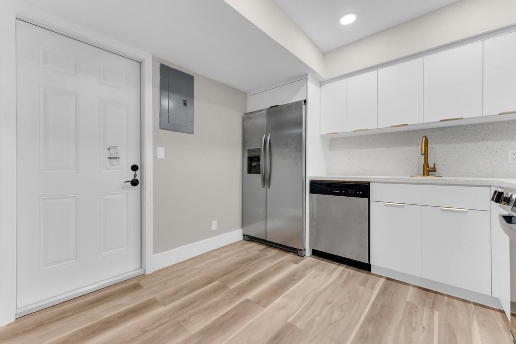 A kitchen features white cabinets, stainless steel appliances, a gold faucet, and light wood flooring — 4281 NW 76th Avenue, Davie FL 33328, DAVIE, FL