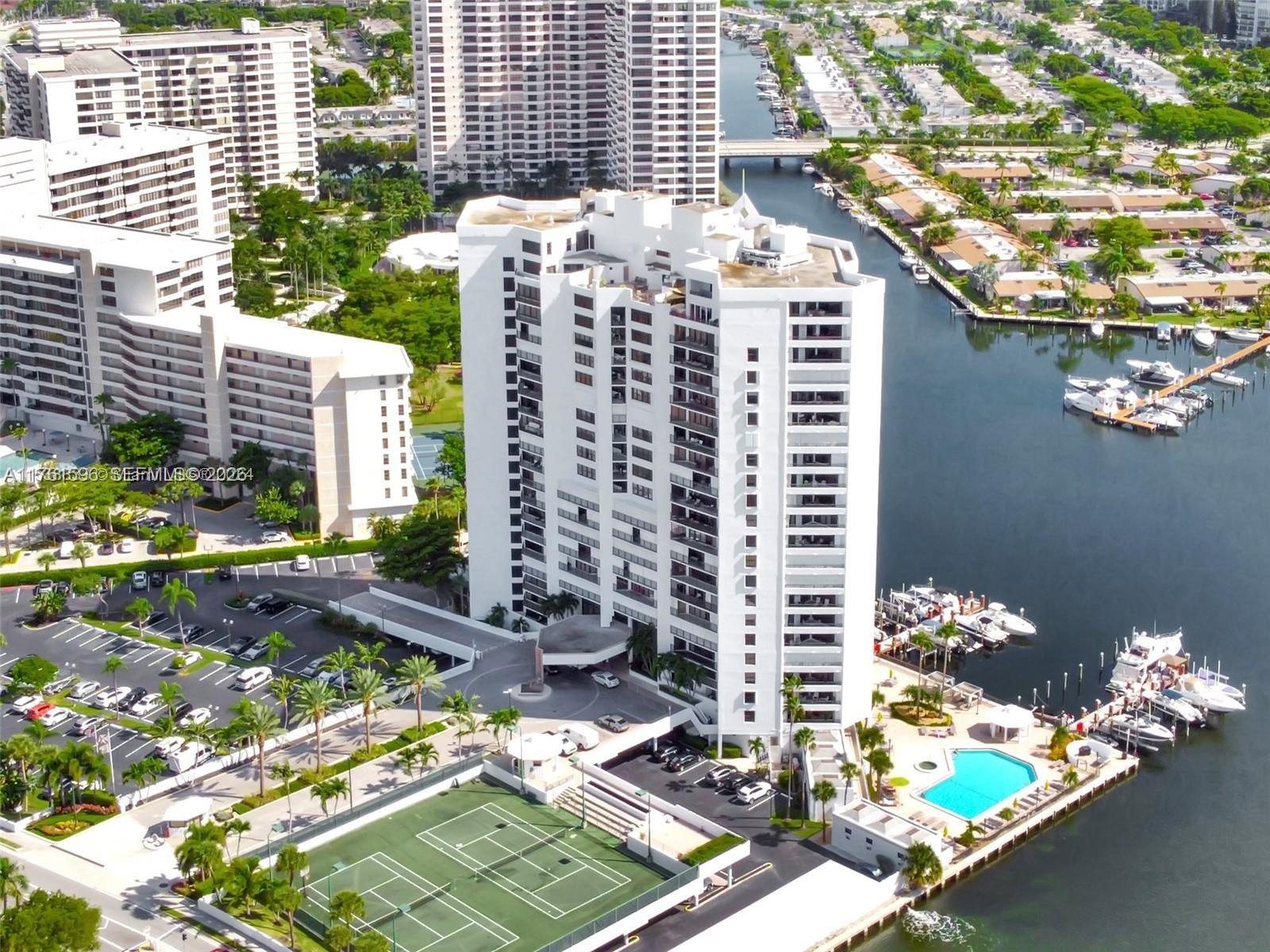 An aerial view shows a white high-rise residential building with a pool, tennis courts, and boats — 300 Three Islands Blvd # 108, Hallandale Beach FL 33009, HALLANDALE BEACH, FL