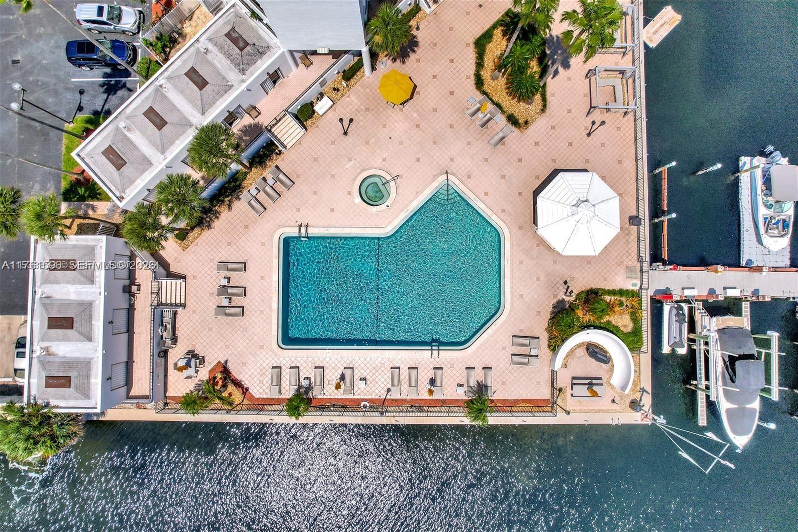 An aerial view shows a swimming pool, hot tub, patio, and boat docks by water — 300 Three Islands Blvd # 108, Hallandale Beach FL 33009, HALLANDALE BEACH, FL
