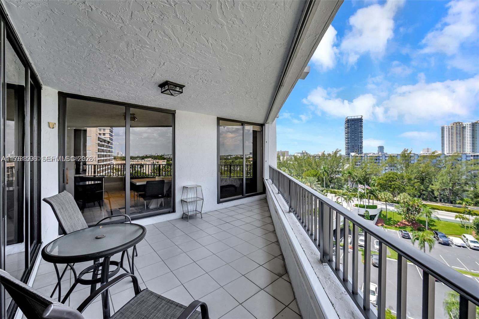 A balcony with tile flooring, metal railings, and a view of surrounding buildings and trees — 300 Three Islands Blvd # 108, Hallandale Beach FL 33009, HALLANDALE BEACH, FL
