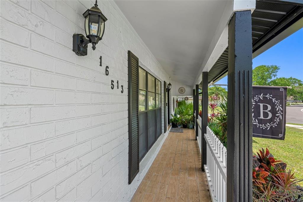 A covered porch with white brick walls, dark shutters, and a wooden-look tiled floor — 16513 SILVERHILL DRIVE, TAMPA, FL