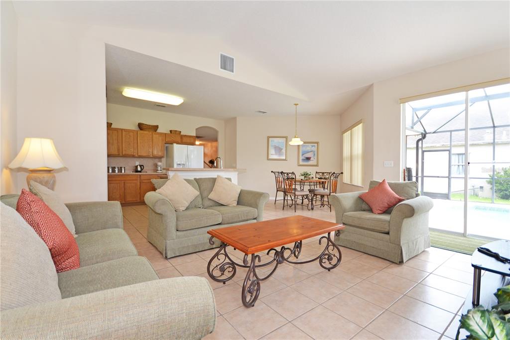 A living room with tile floors, green sofas, and a view of a screened-in patio — 423 CORVINA DRIVE, DAVENPORT, FL