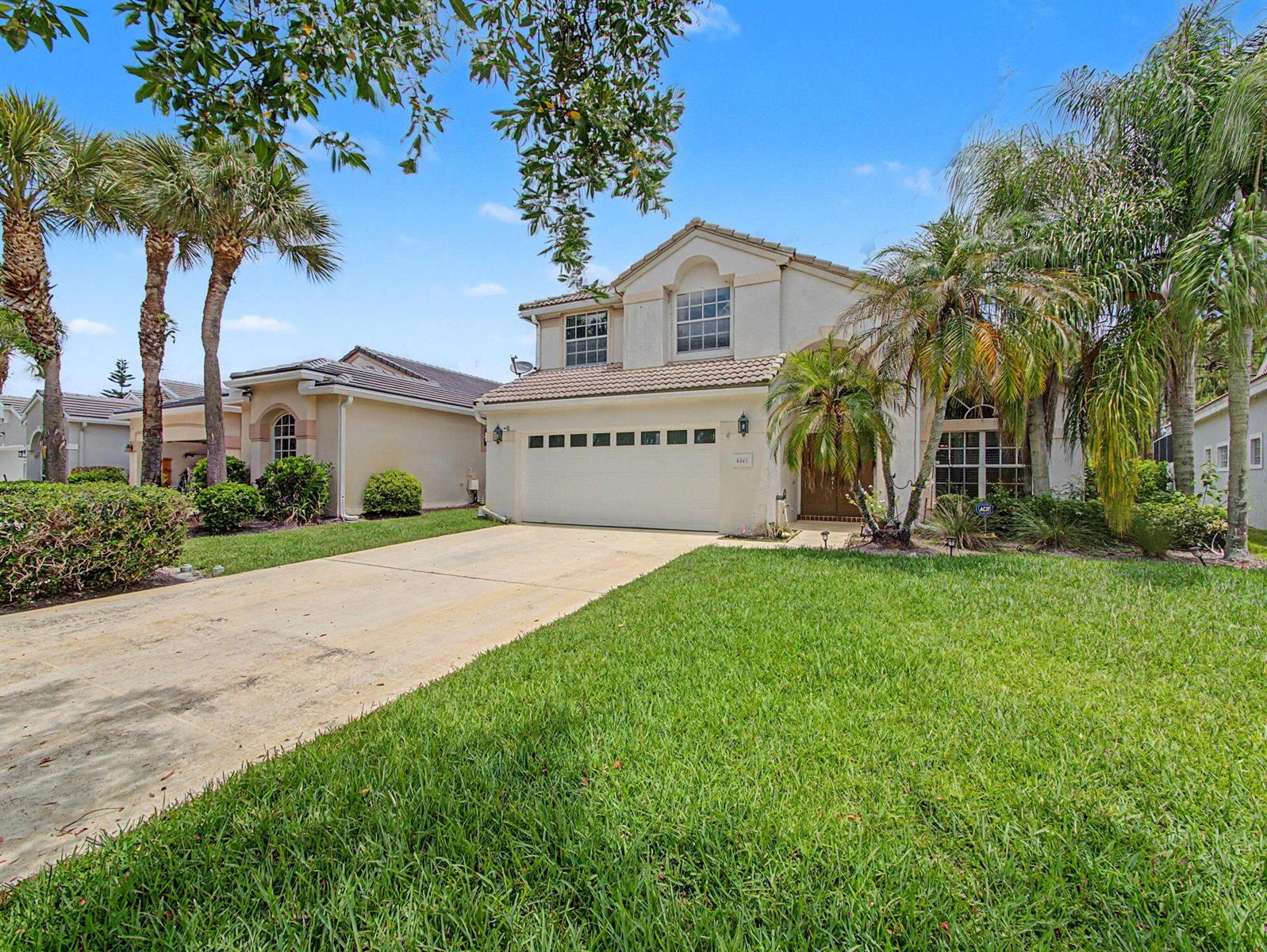 A two-story suburban house with a concrete driveway, a two-car garage, and palm trees — 6467 SE Wild Olive Lane, Stuart FL 34997, STUART, FL