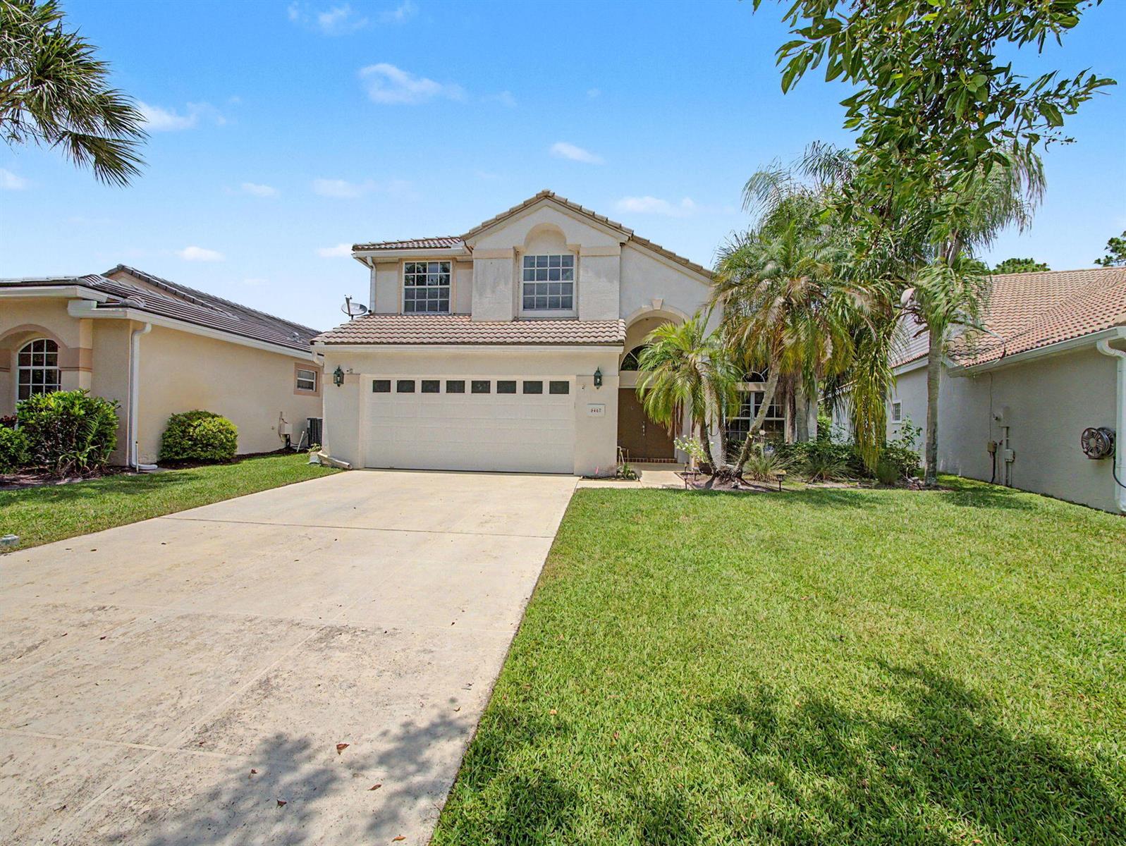 A two-story suburban house with a beige stucco exterior, a two-car garage, and palm trees — 6467 SE Wild Olive Lane, Stuart FL 34997, STUART, FL