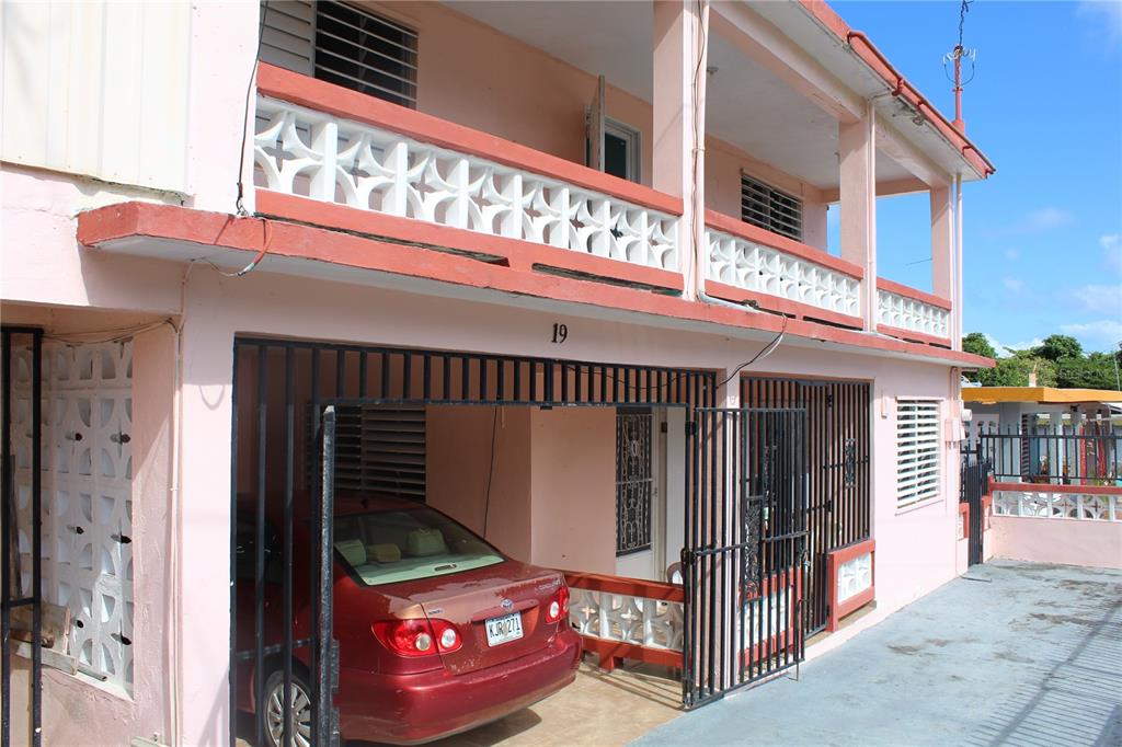 A two-story pink house with a carport, a balcony, and a red sedan parked underneath — 19 CALLE CORAL, VIEQUES, PR