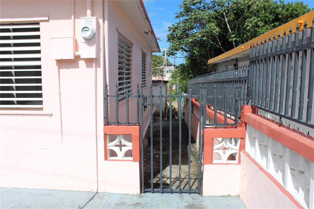 A narrow gated walkway sits between a pink house and a decorative concrete wall — 19 CALLE CORAL, VIEQUES, PR