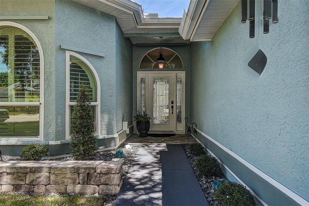 A light blue stucco house features an arched entryway with a glass-paneled front door — 1105 CLIPPERS WAY, TARPON SPRINGS, FL